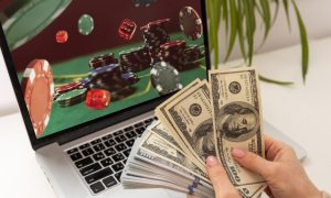 Image of hands holding cash in front of a computer for a story on New Jersey online casinos looking to set another revenue record in April.