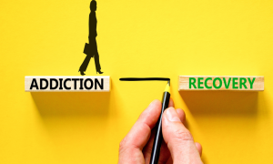 a hand connecting addiction to recovery over a yellow board