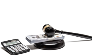 a calculator next to a gavel under a stack of hundred dollar bills