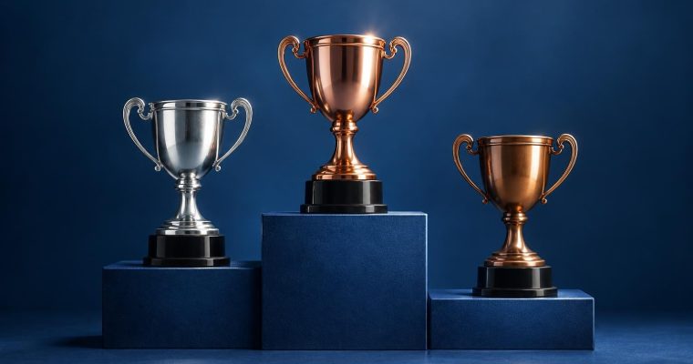 Three championship trophies, one silver and two bronze, are displayed on a blue stepped podium against a dark blue background.