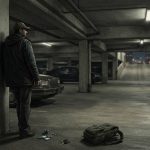 An illustrated figure in a cap and coat stands in a dimly lit parking garage near a backpack, some loose items, and parked cars.